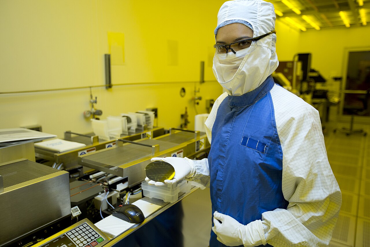 A researcher inspects a patterned silicon wafer in a fabrication lab